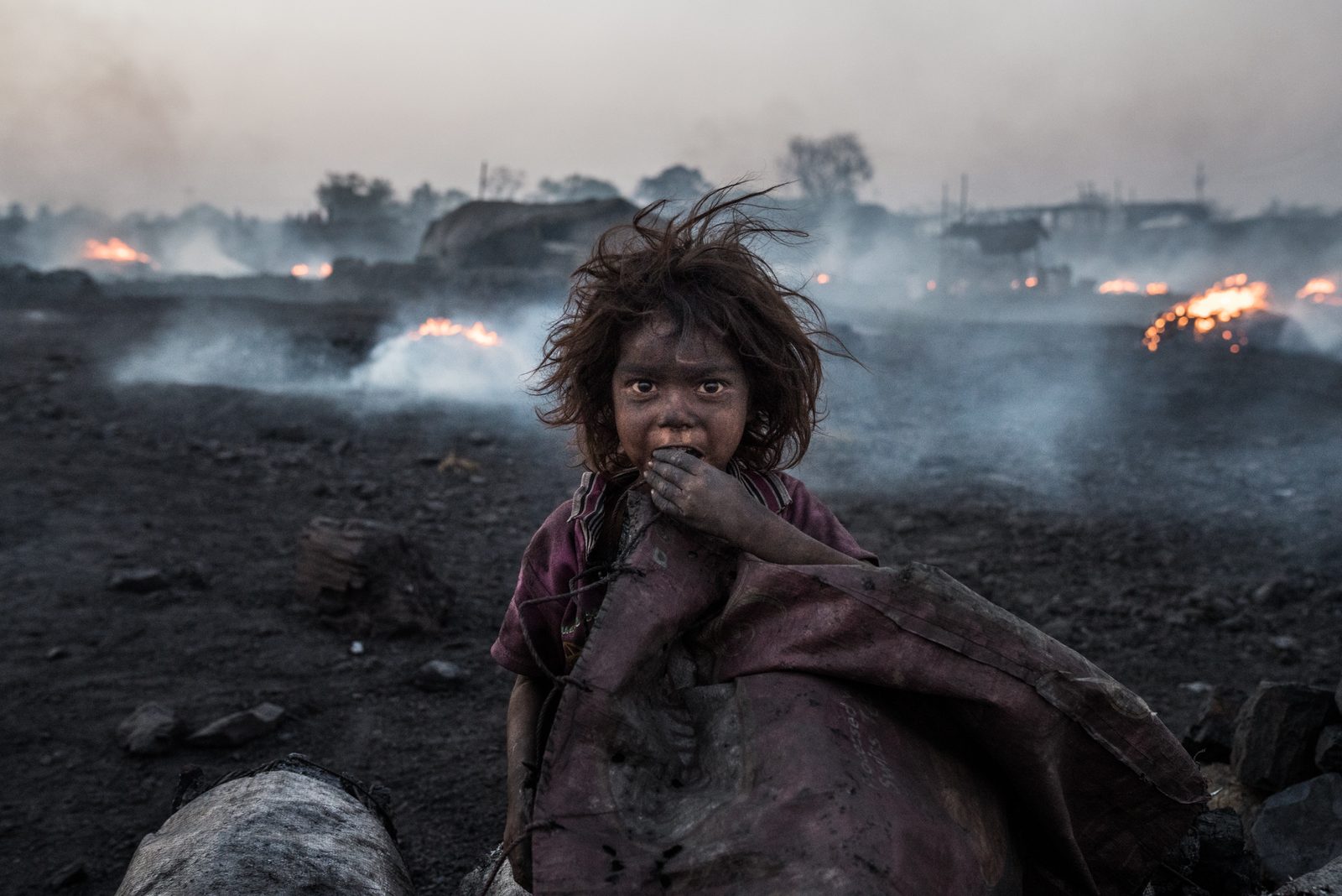 A child waits for her parents as they work in the charcoal production fields of Jharkhand, India
