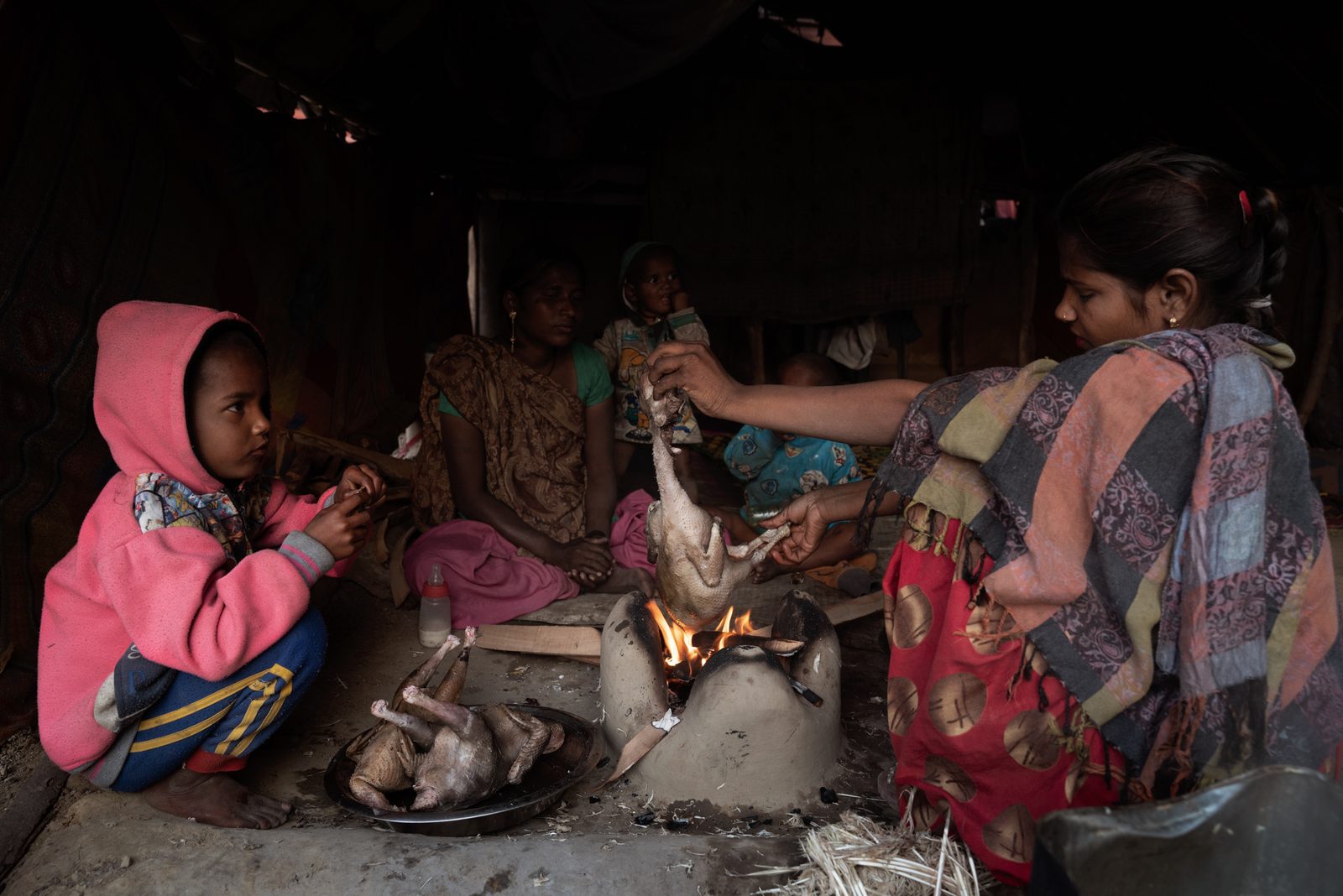 A migrant family cooks chicken over an open fire on the outskirts of New Delhi, India