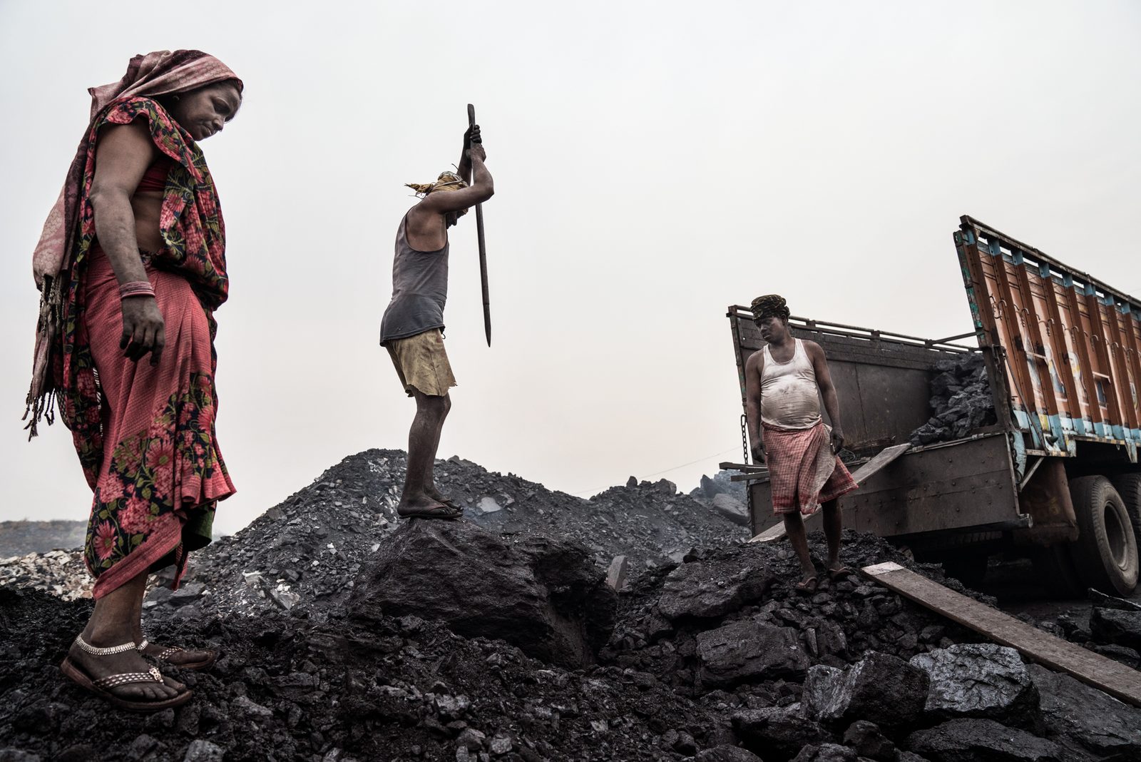 Coal mine workers break up large pieces of coal used to power cities and factories across India
