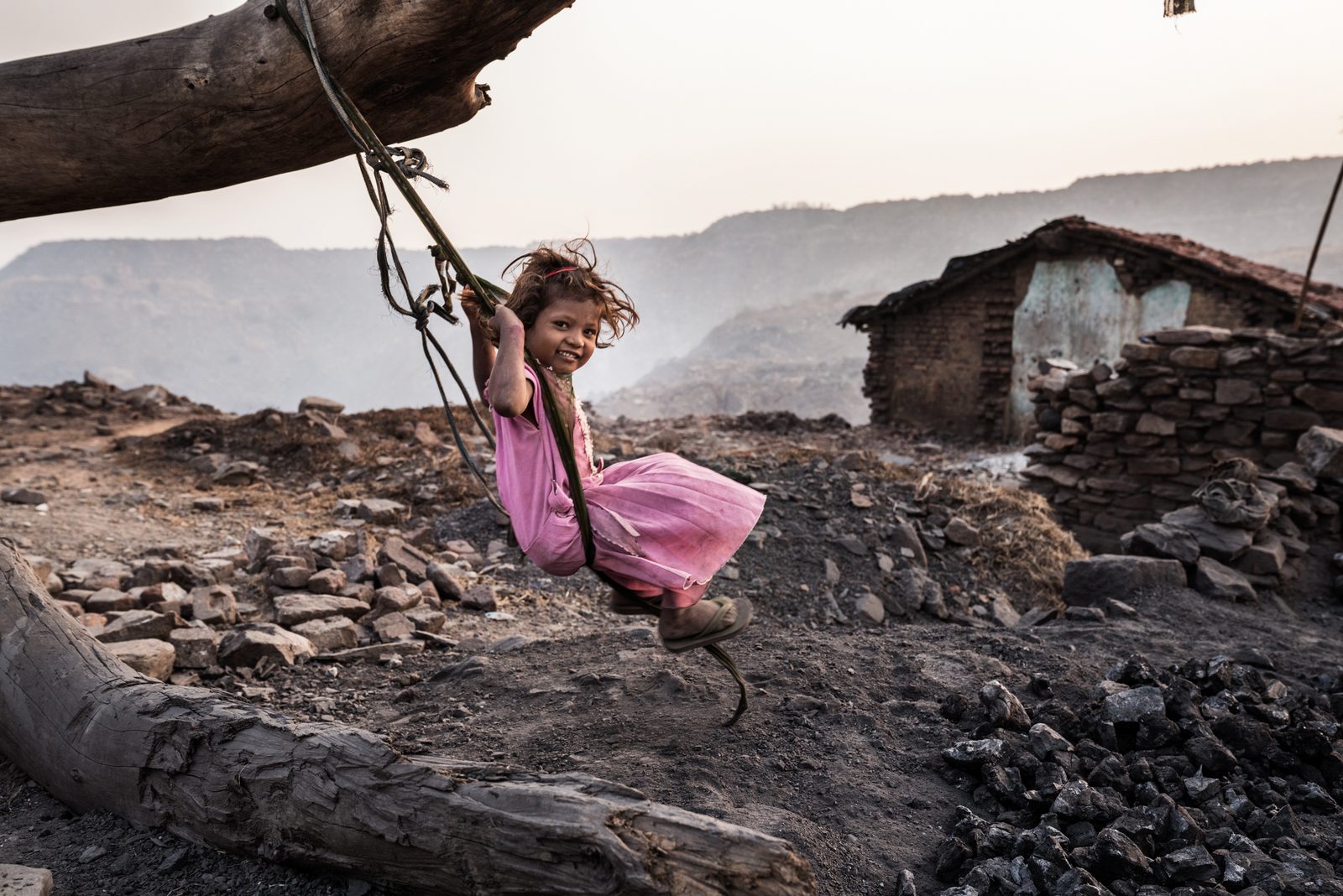 A young girl swings off a dead tree outside her home - one of the last remaining homes yet to collapse from the underground coal-sea fire in Jharkhand, India