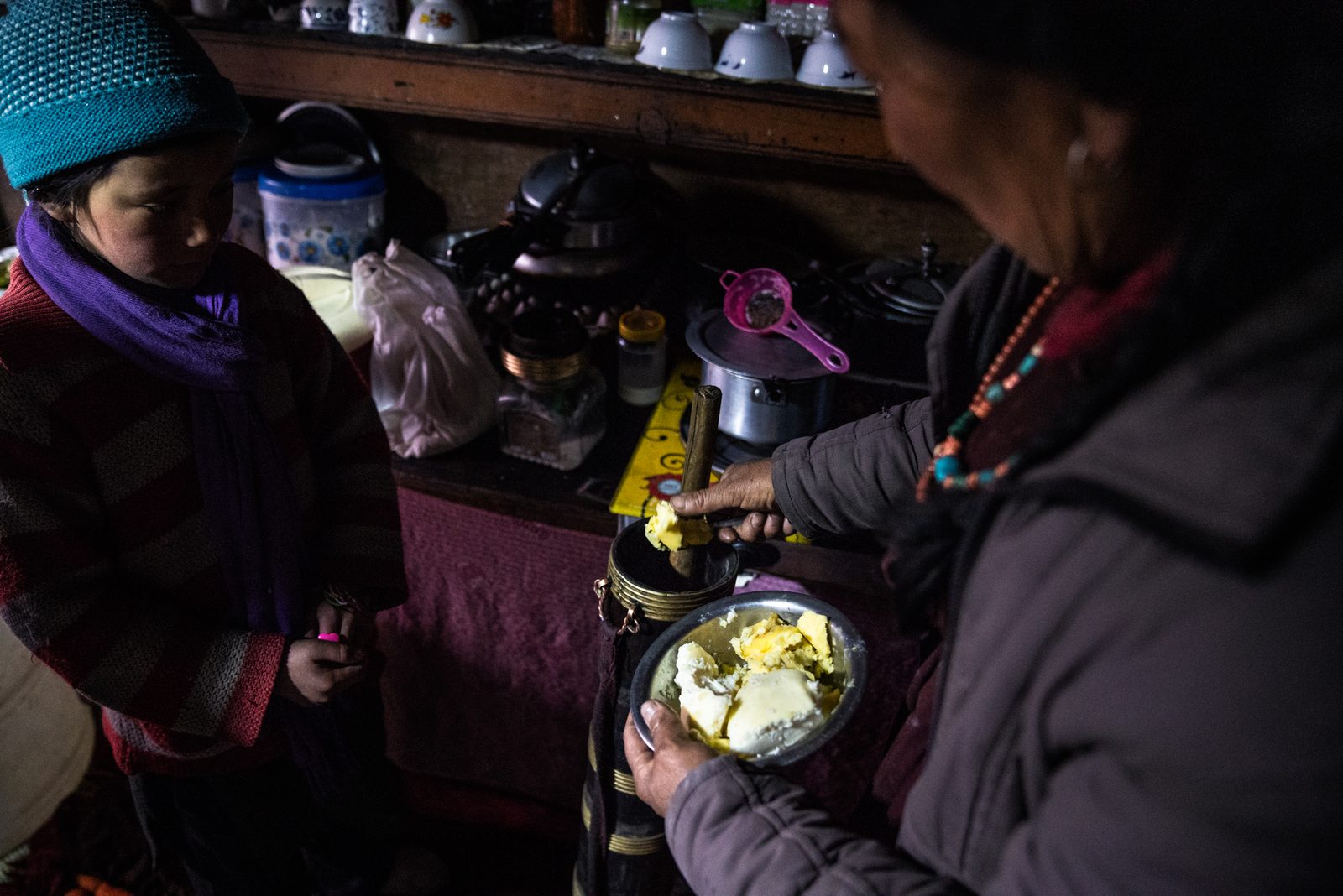 Tsewang Putit spoons locally made butter into a traditional butter tea masher, along with salt and hot water to make butter tea