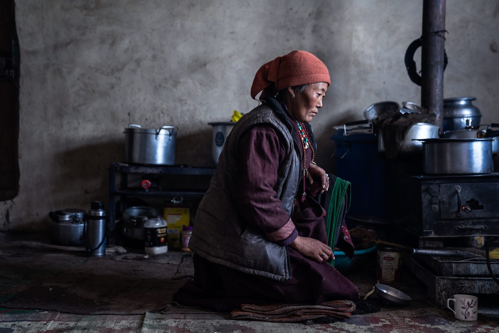 A woman sits by the stove waiting for a serving of butter tea