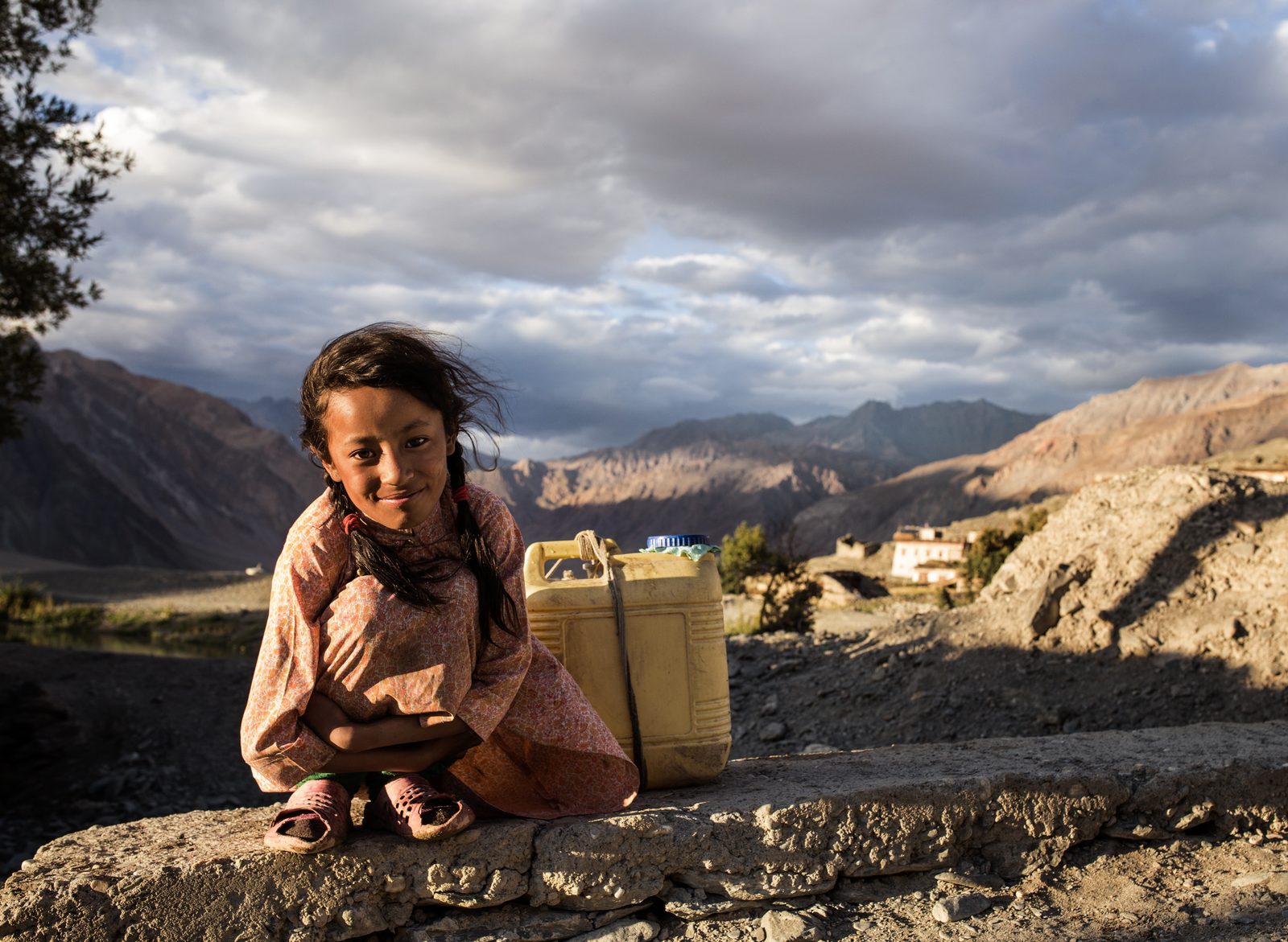 A young girl takes a break while she walks home with her water-filled jerry cans