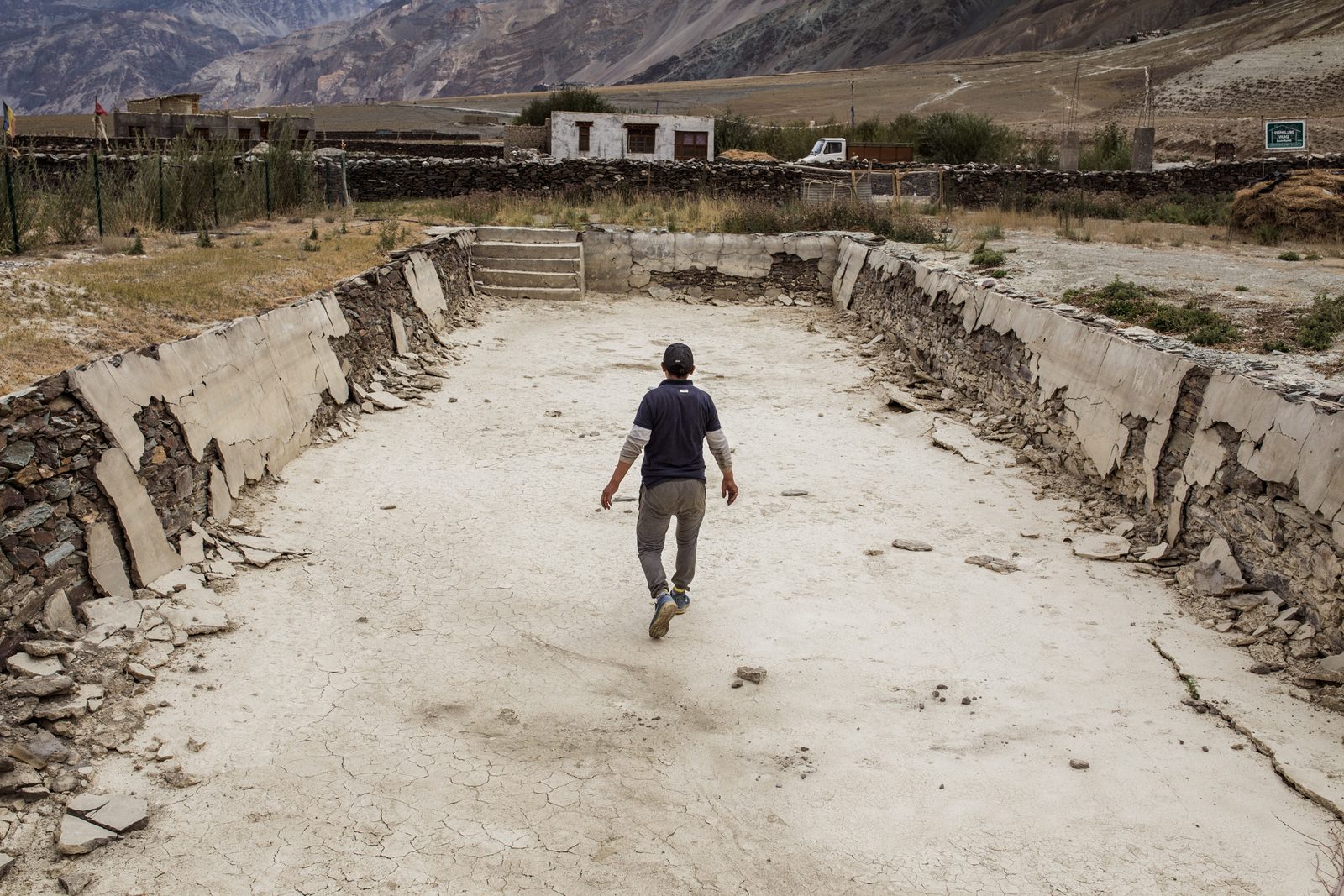 Tashi Stobdan walks through his empty and crumbling water storage pool next to his new house in Lower Kumik